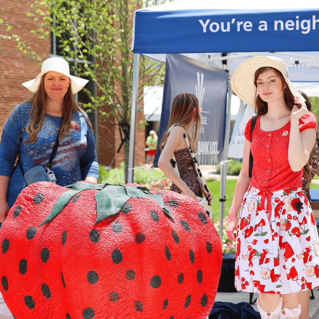 two woman standing next to a large strawberry