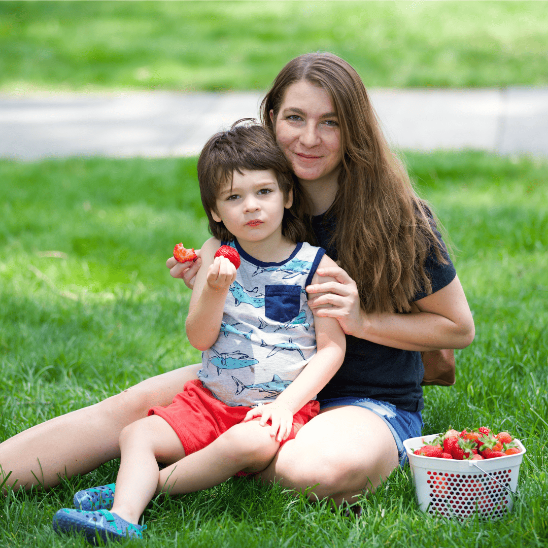 Young woman and a child eating strawberries on the grass