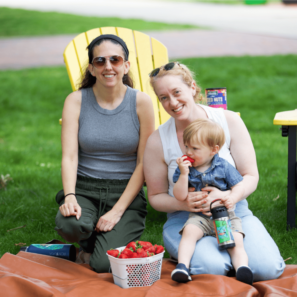 Two women and a child eating strawberries on a blanket